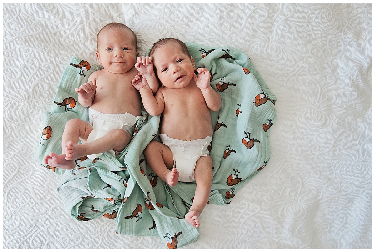 Newborn twin baby boys lie on a muslin blanket together
