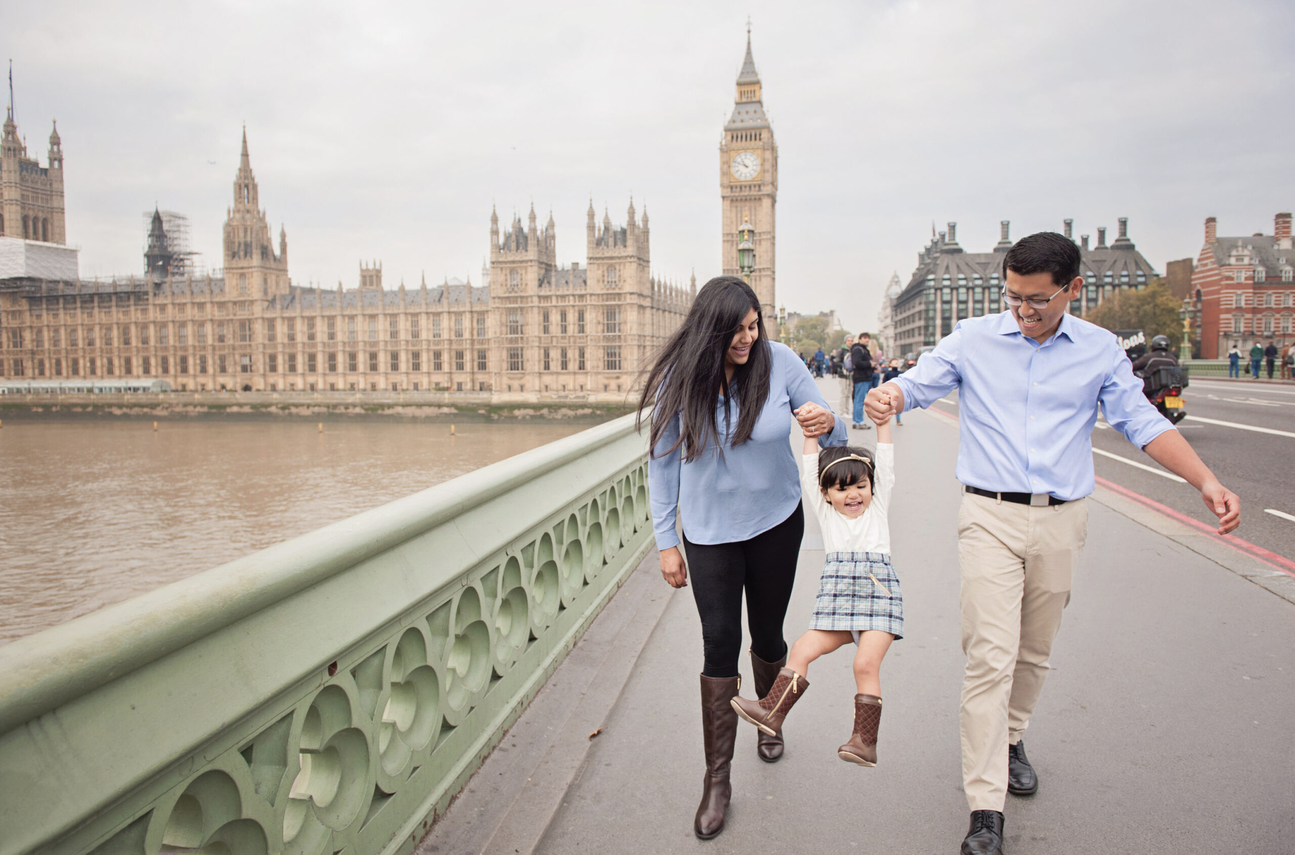A family swing their little girl on Westminster Bridge during a London vacation photo shoot with Big Ben and the House of Parliament in the background.
