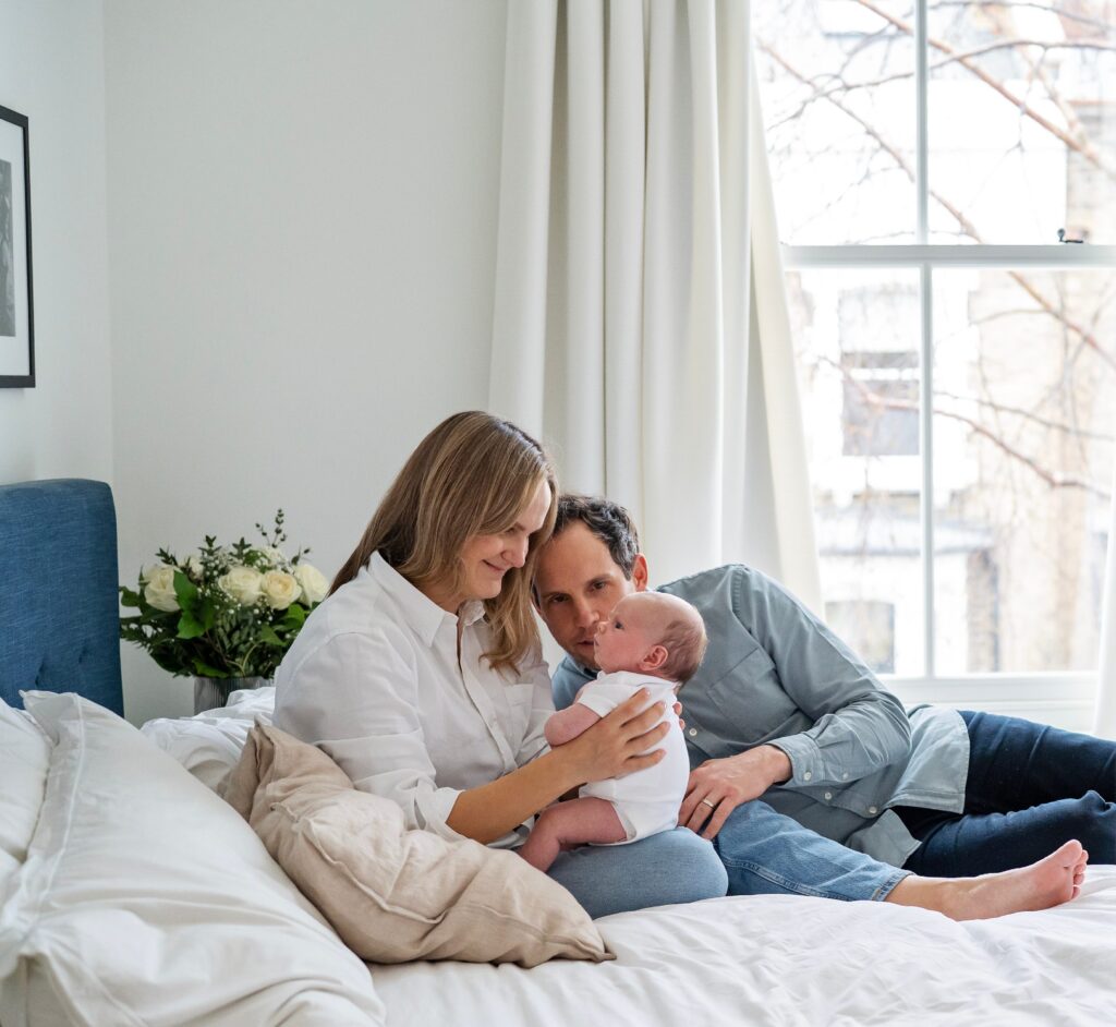 New mother and father sit on their bed cuddling their new baby girl