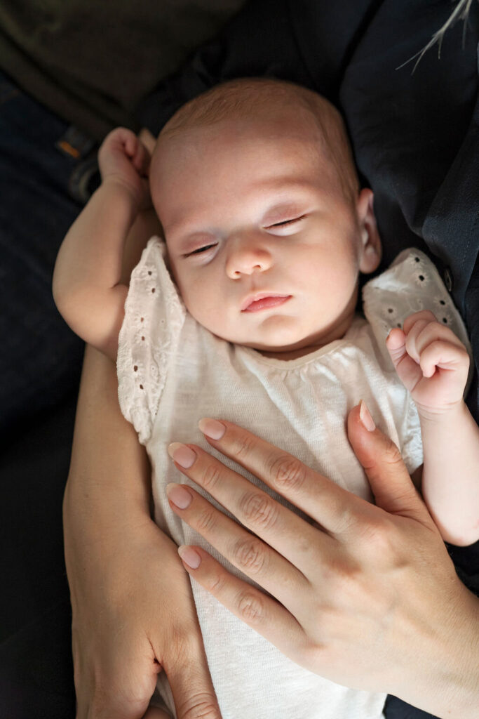 Photo of an older newborn fast asleep in her mum's arms while she poses for a newborn photo shoot