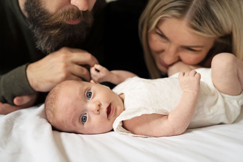 Photo of an older newborn lying down in front of her mum and dad while she poses for a newborn photo shoot