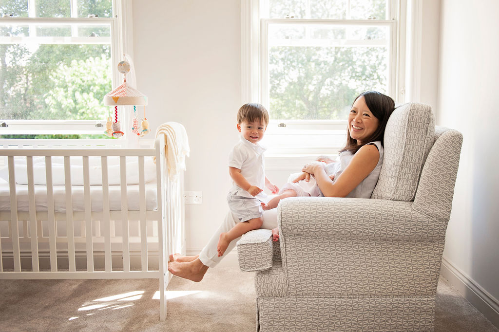 A mother sitting with her newborn and older child posing for an at home newborn photoshoot