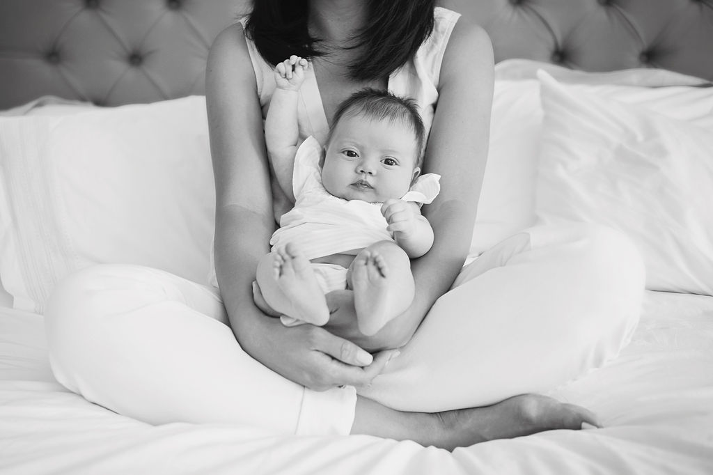 A mother sitting on the bed holding her newborn baby for an at home photoshoot