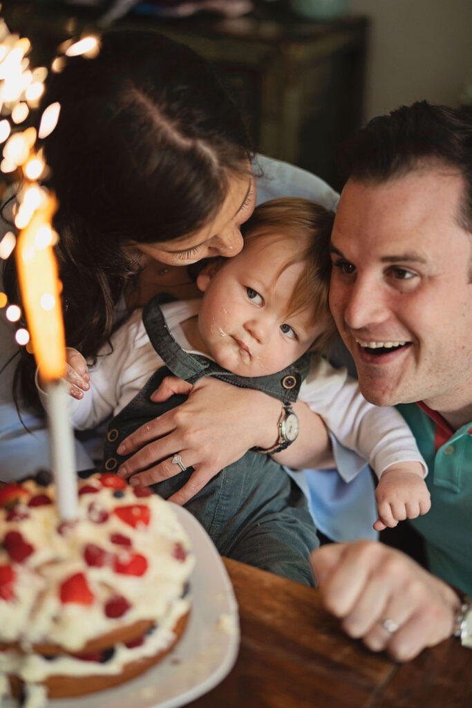 Picture of a birthday cake and family of three. They are posing for an alternative cake smash photo session.