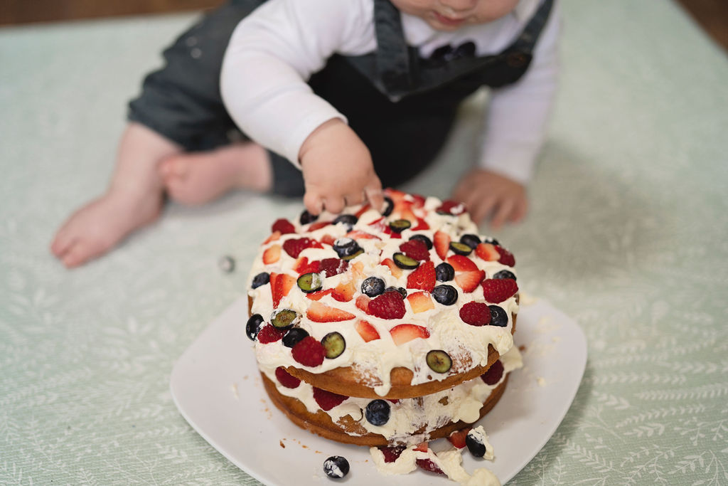 Picture of a one year old with his finger in his birthday cake. They are posing for an alternative cake smash photo session.