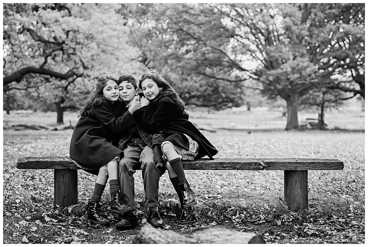 Image of three young children sitting on a park bench for an autumn photo shoot in Richmond Park, London