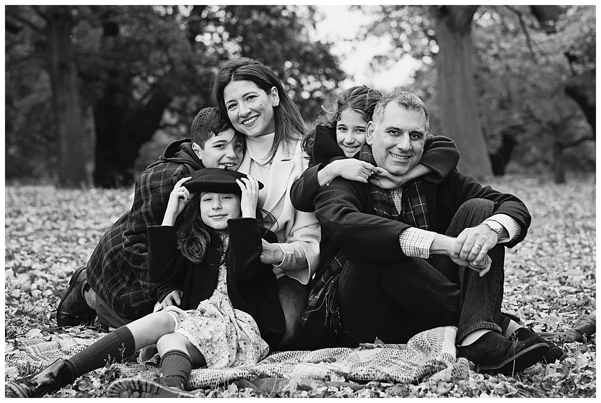 Image of a family sitting on some autumn leaves in Richmond Park. This image is to give readers some Autumn Photoshoot Outfit Ideas