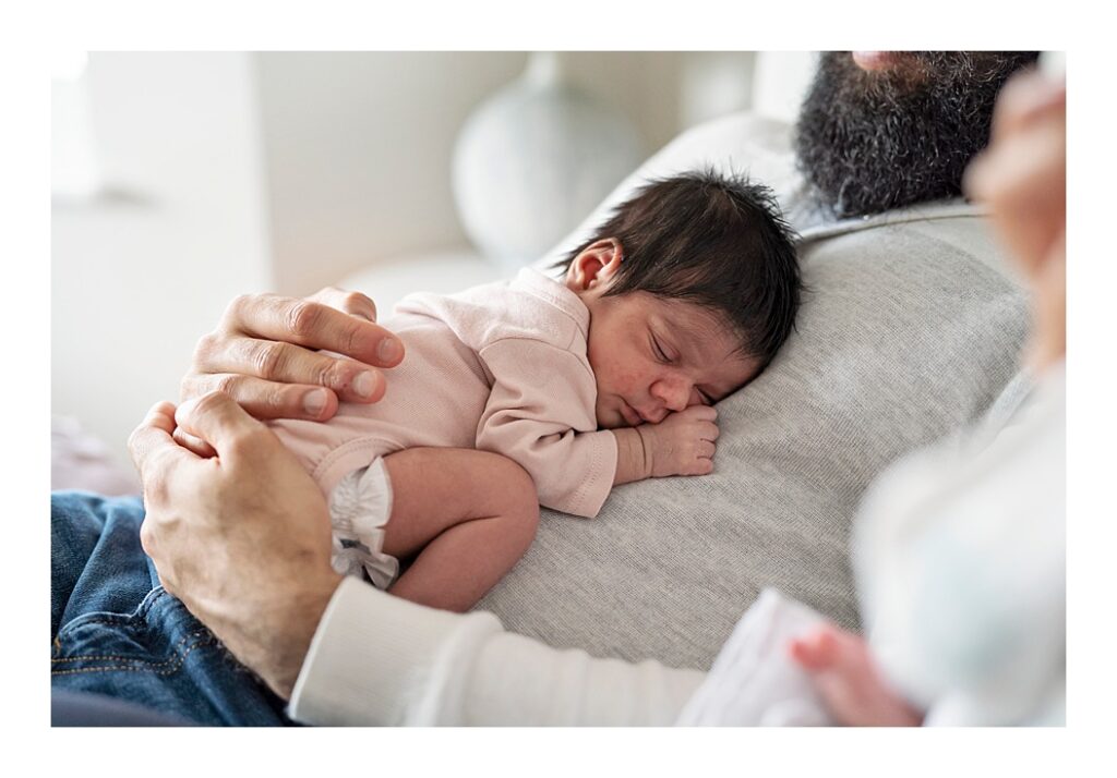 A sleeping newborn baby girl rests on her father's chest.

