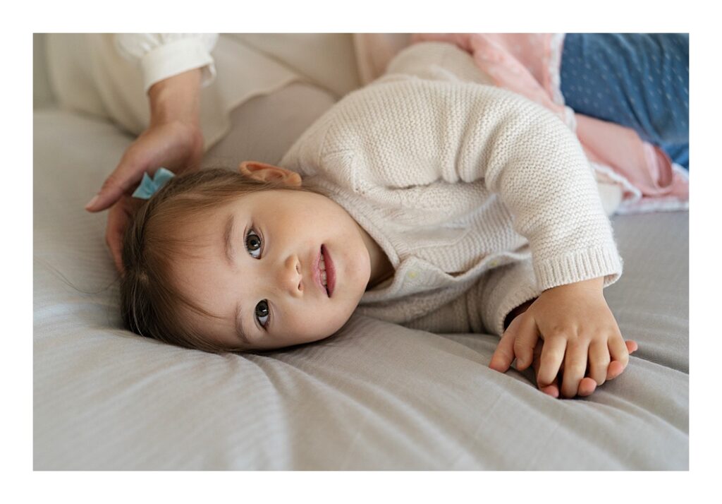Toddler girl resting head on bed during photo shoot to celebrate her mother's second pregnancy.
