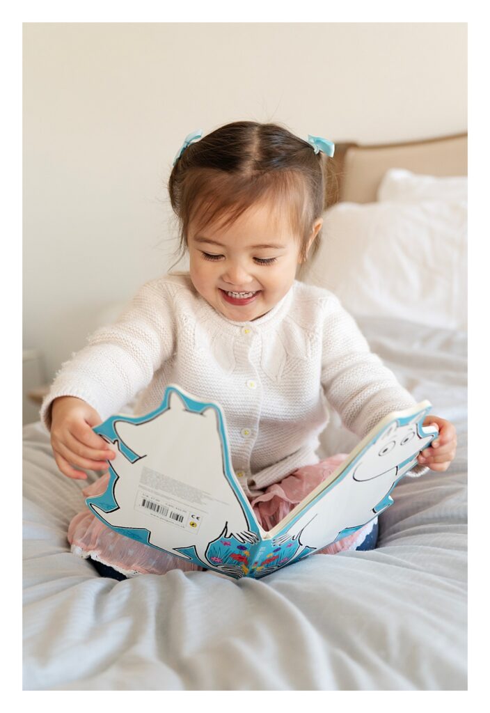 2 year old little girl reading a Moomin book