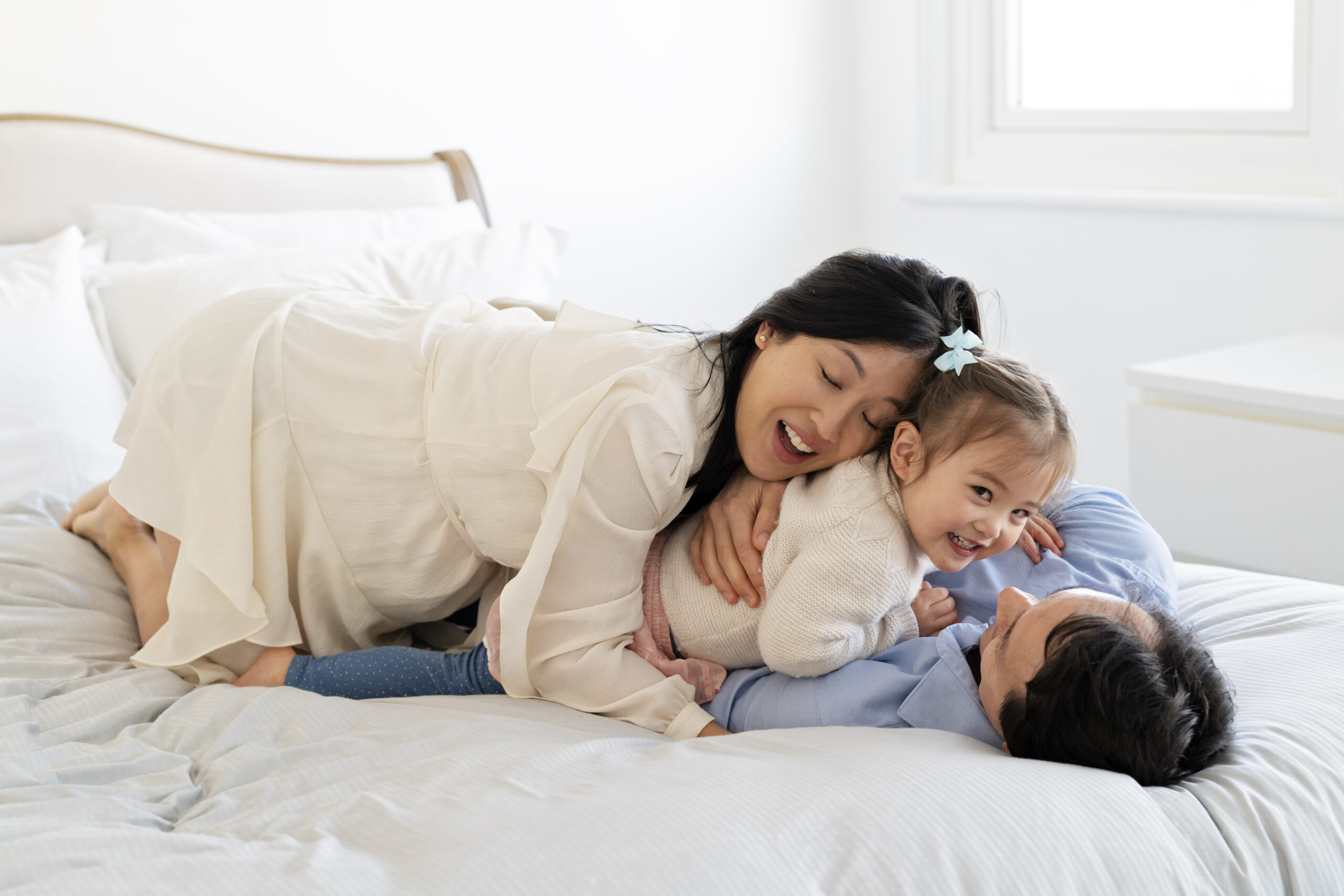 Family bundle and play together on the bed during a family maternity photo shoot with Jess Morgan