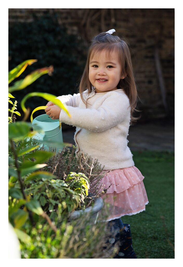 Toddler girl wearing a pink tutu skirt waters the garden with her blue watering can
