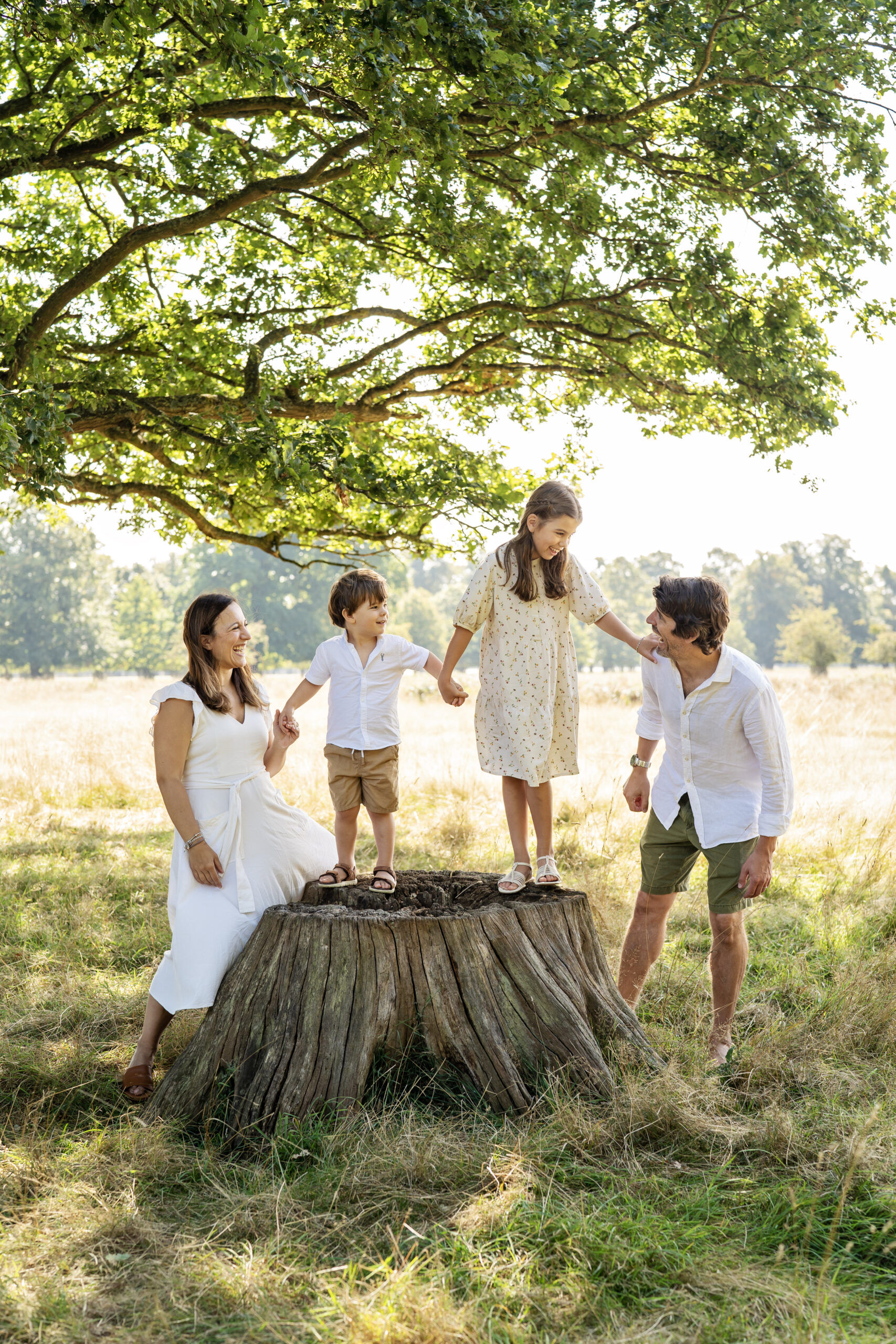 A family stand on an old tree stump holding hands during a family photo shoot in London's Bushy Park