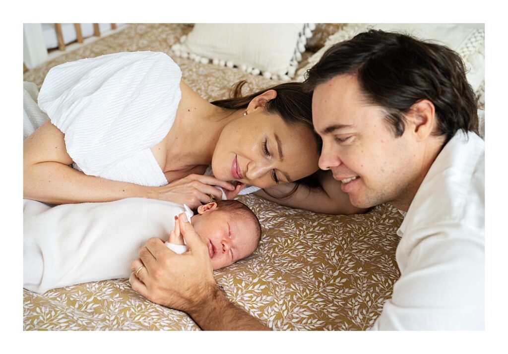 Mother and father rest on their bed with sleeping baby boy