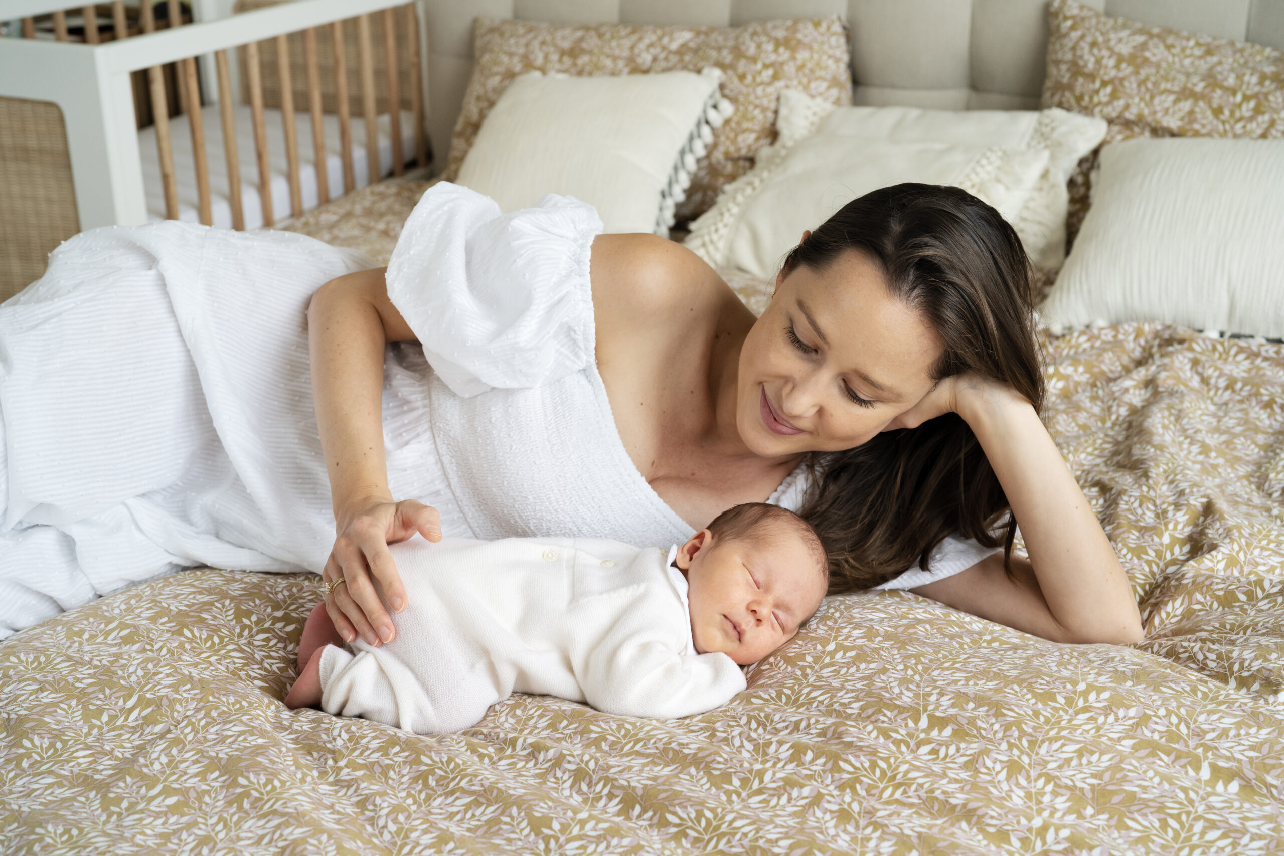 A new mother on the bed with her sleeping baby during an at-home newborn photo shoot with Jess Morgan Photography