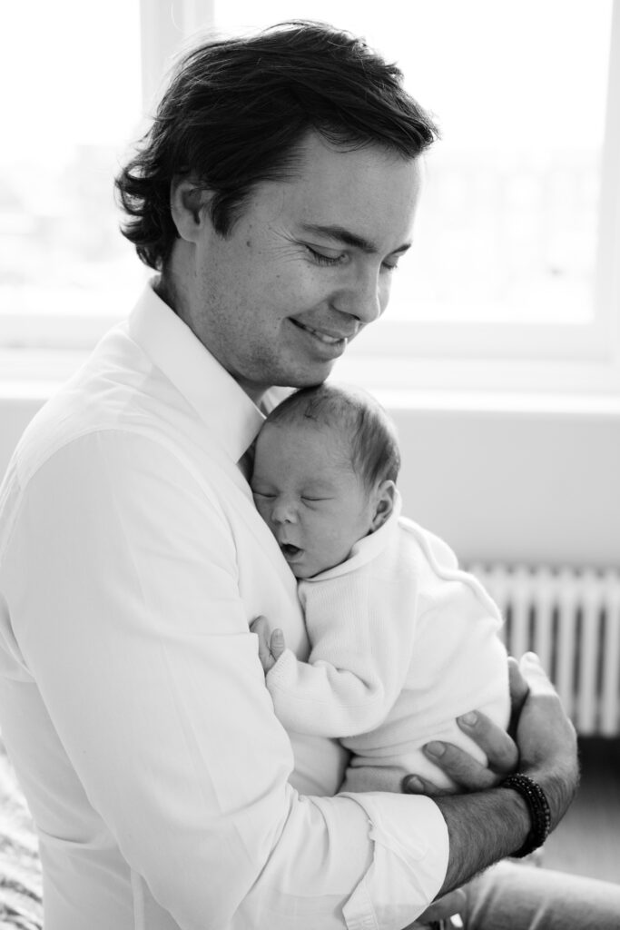 Father smiles as he holds his new baby boy asleep against his chest