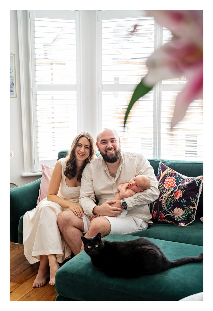 couple sit on a sofa for with their 8 week old baby boy for a newborn photo shoot at their London home.